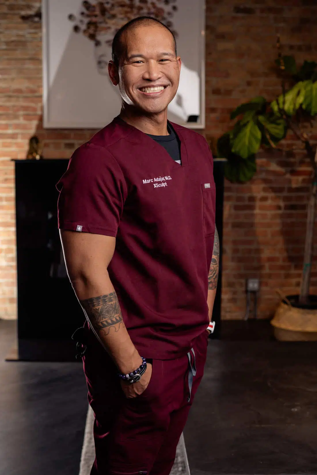 A man in scrubs smiling in front of a brick wall showcasing abdominal etching.