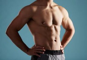 Closeup, shirtless and man in studio, muscular and fitness on blue background. Person, healthy physique and model with pecs, confidence and workout with training, bodybuilder and results for exercise.