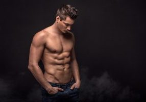 Handsome shirtless man posing on black studio background.